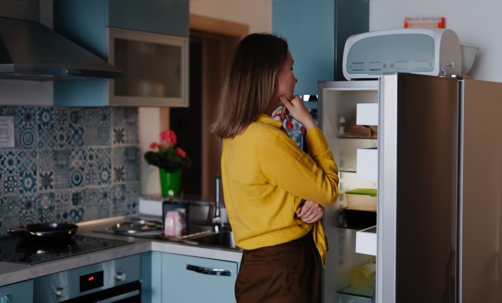 Woman looking inside an open fridge while deciding what to eat.